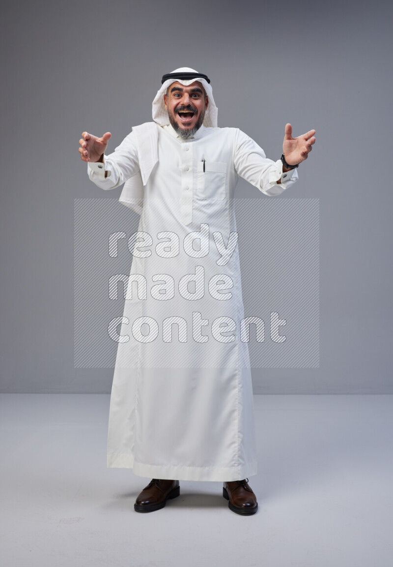 Saudi man Wearing Thob and white Shomag standing interacting with the camera on Gray background