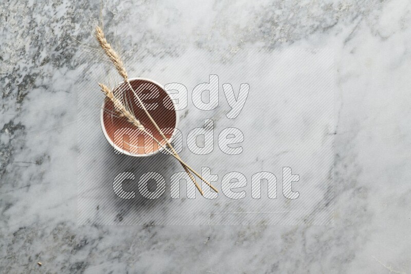 Wheat stalks on brown pottery bowl on grey marble background