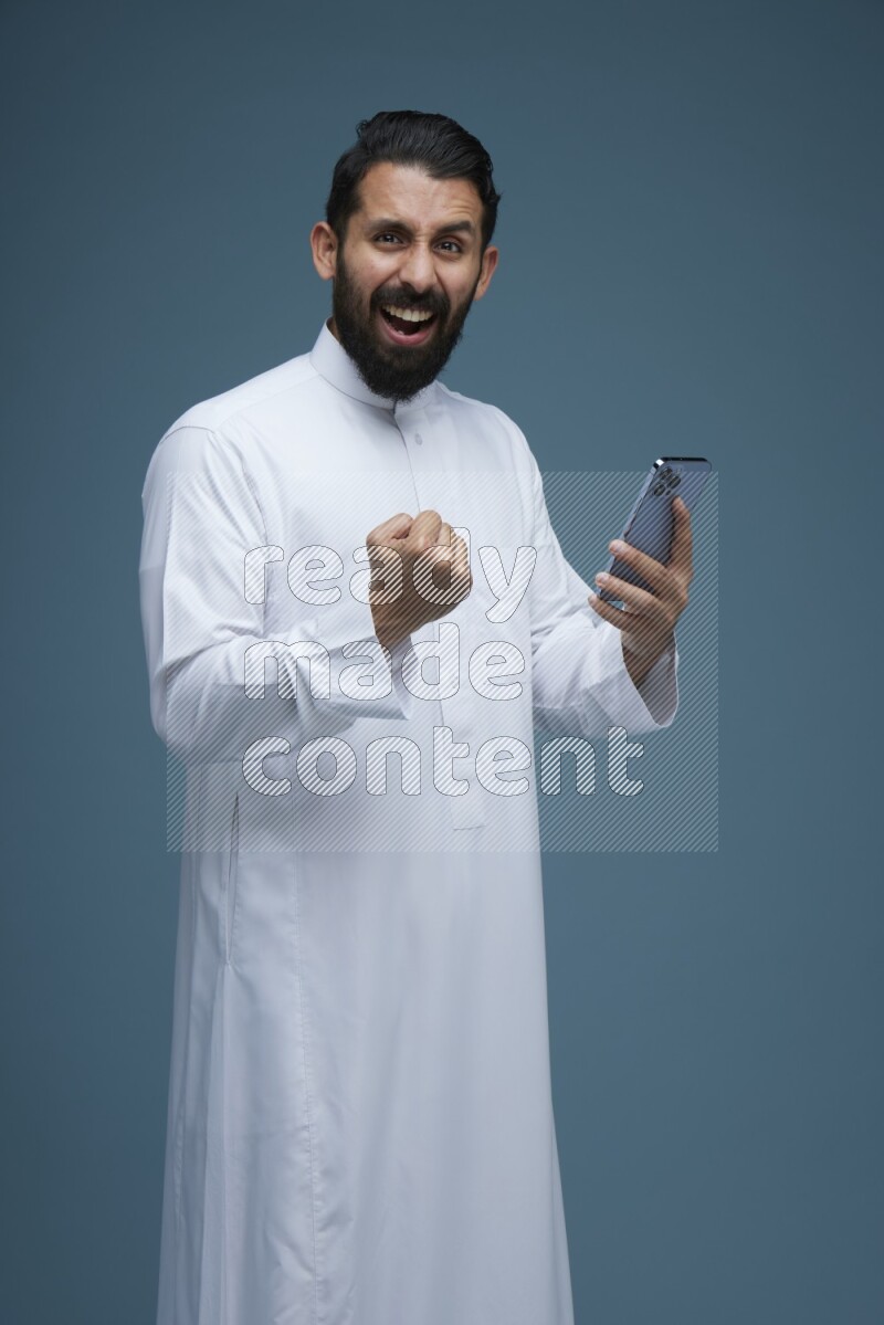 A man Texting in a blue background wearing Saudi Thob