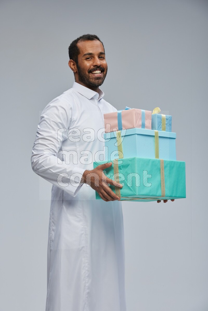 Saudi man Wearing thob standing holding gift box on Gray background
