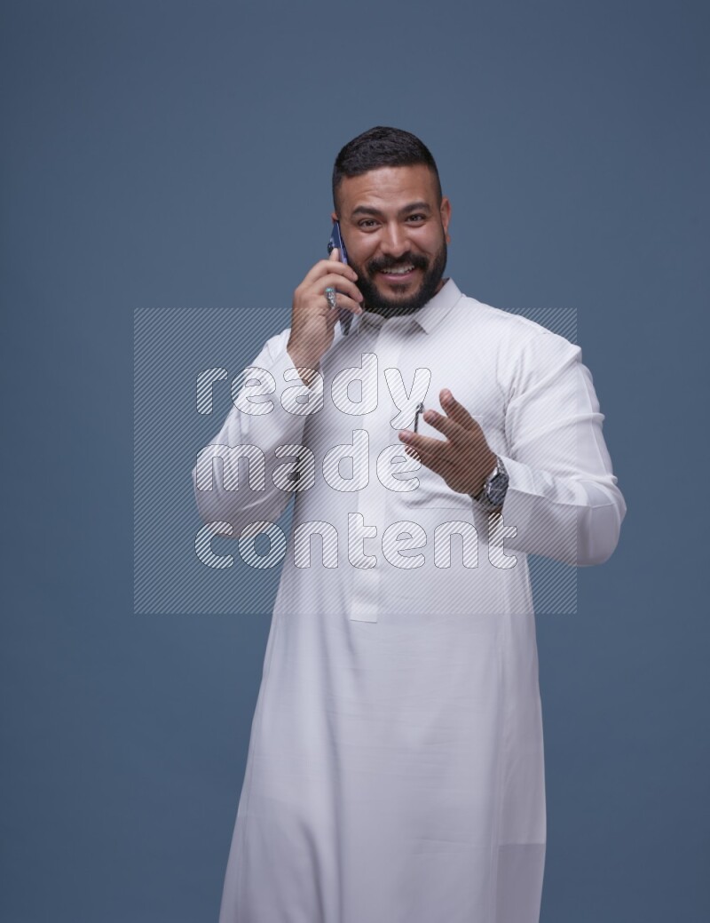 A Saudi man calling on blue background wearing Saudi Thob