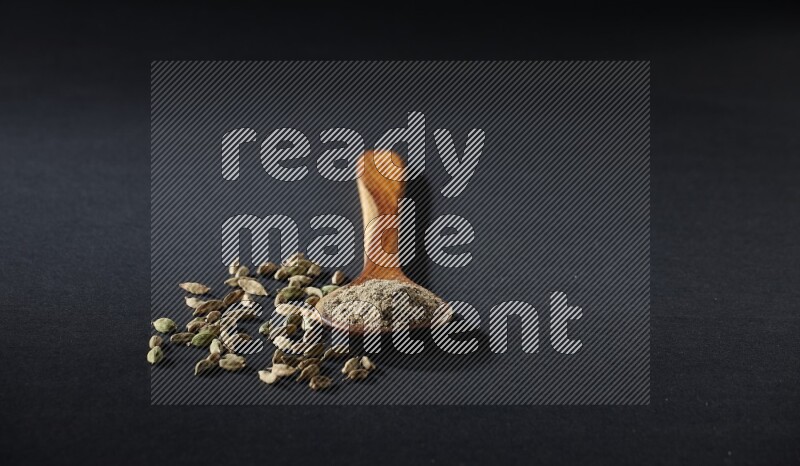 مغرفة خشبية ممتلئة ببودرة الهيل وحبوب الهيل بجانبها على خلفية سوداء