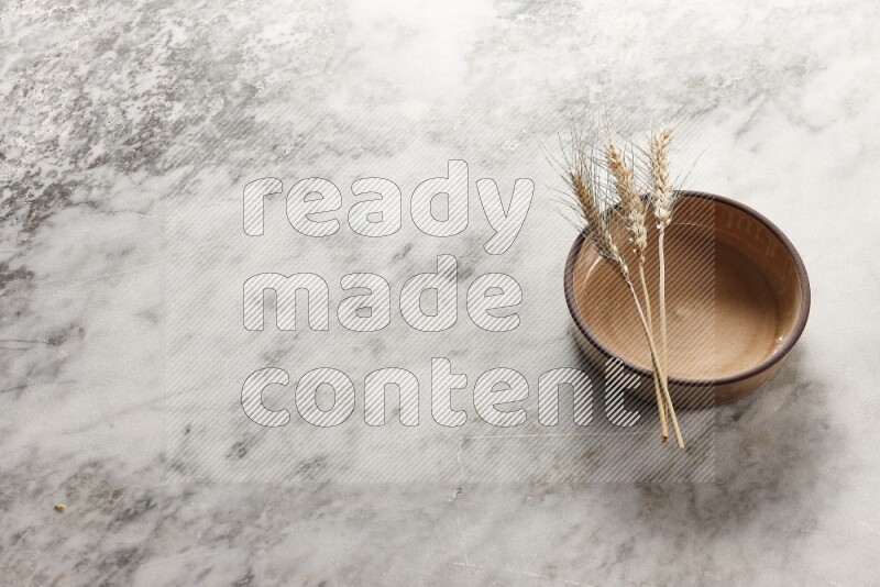 Wheat stalks on beige pottery oven bowl on grey marble background