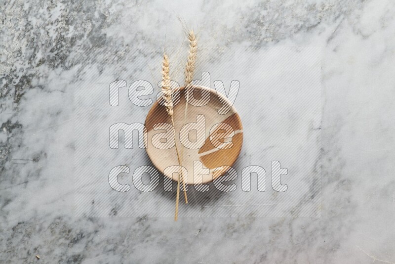 Wheat stalks on multicolored pottery plate on grey marble background