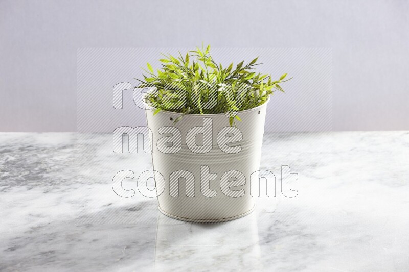 Green artificial plant in white pot on light grey marble background