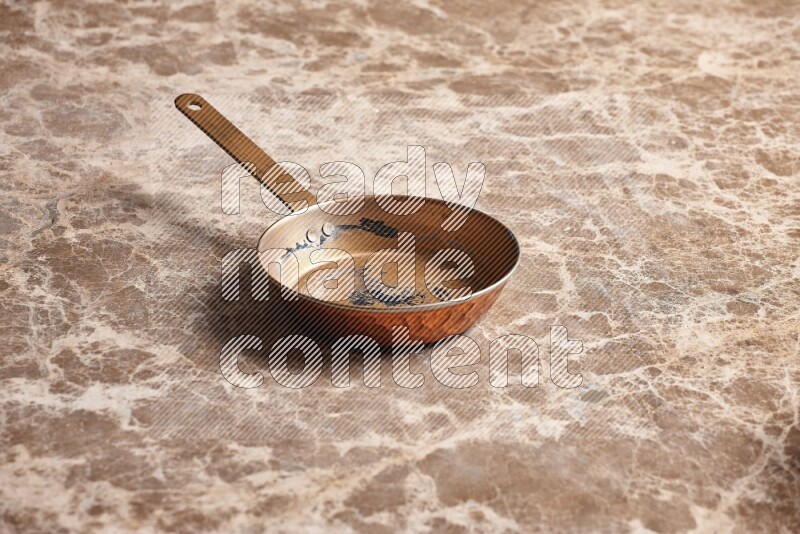 A small copper pan on beige marble background