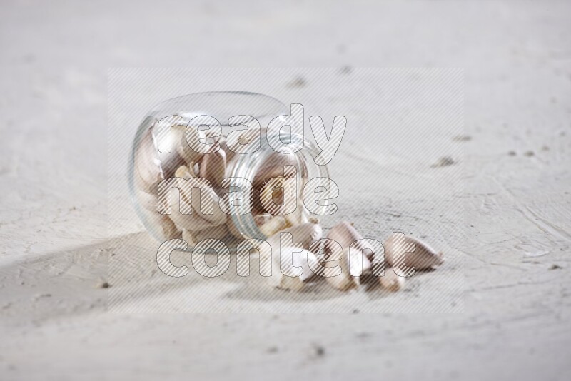 A glass spice jar full of garlic cloves flipped over with the cloves spilling out on a textured white flooring