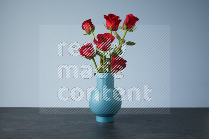 An arrangement of vivid red roses in a blue vase on black marble background
