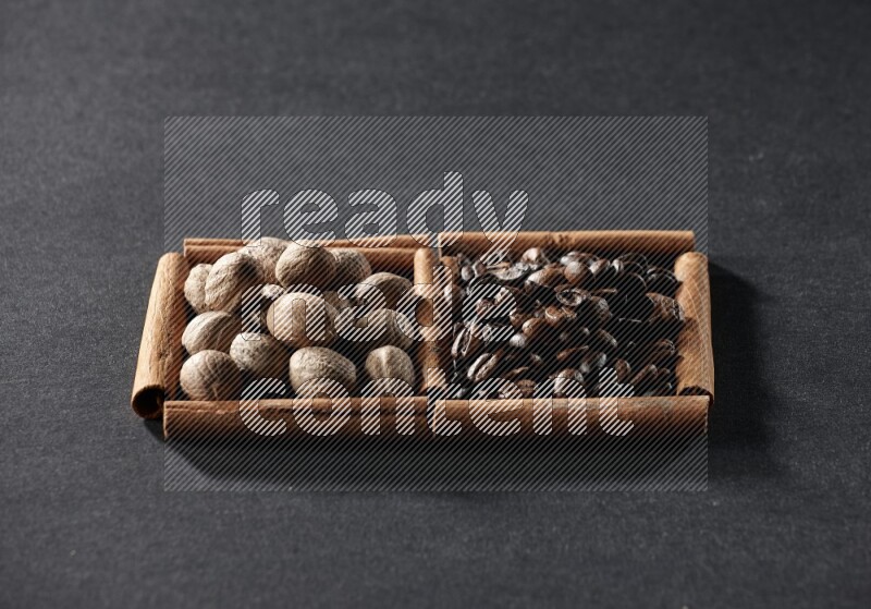 مربعان من أعواد القرفة ممتلئان بحبوب القهوة وجوزة الطيب علي خلفية سوداء