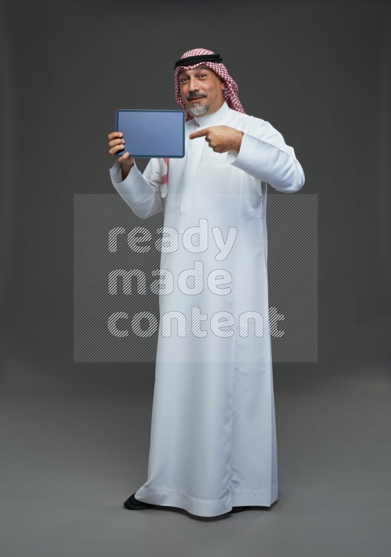 Saudi man with shomag Standing working on tablet on gray background