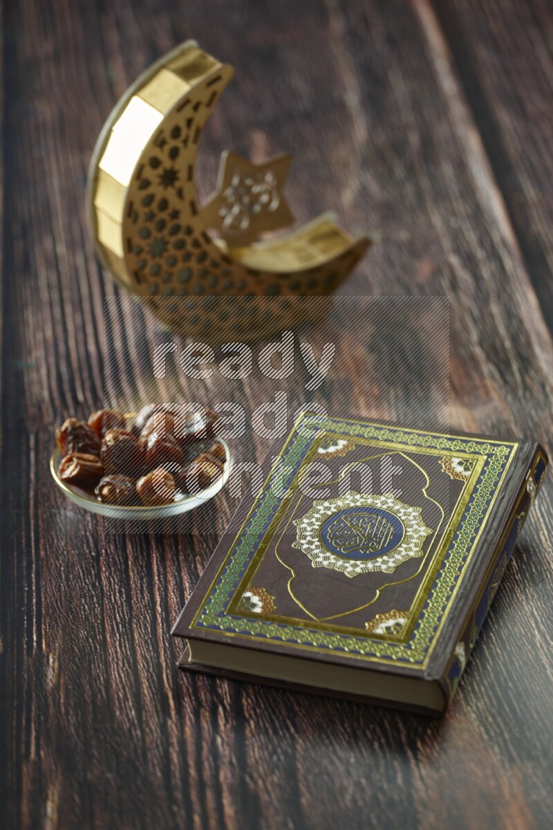 A wooden golden crescent lantern with different drinks, dates, nuts, prayer beads and quran on brown wooden background
