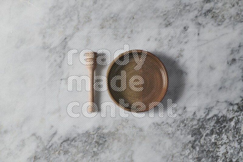 Multicolored pottery oven plate with wooden honey dipper on the side on grey marble background