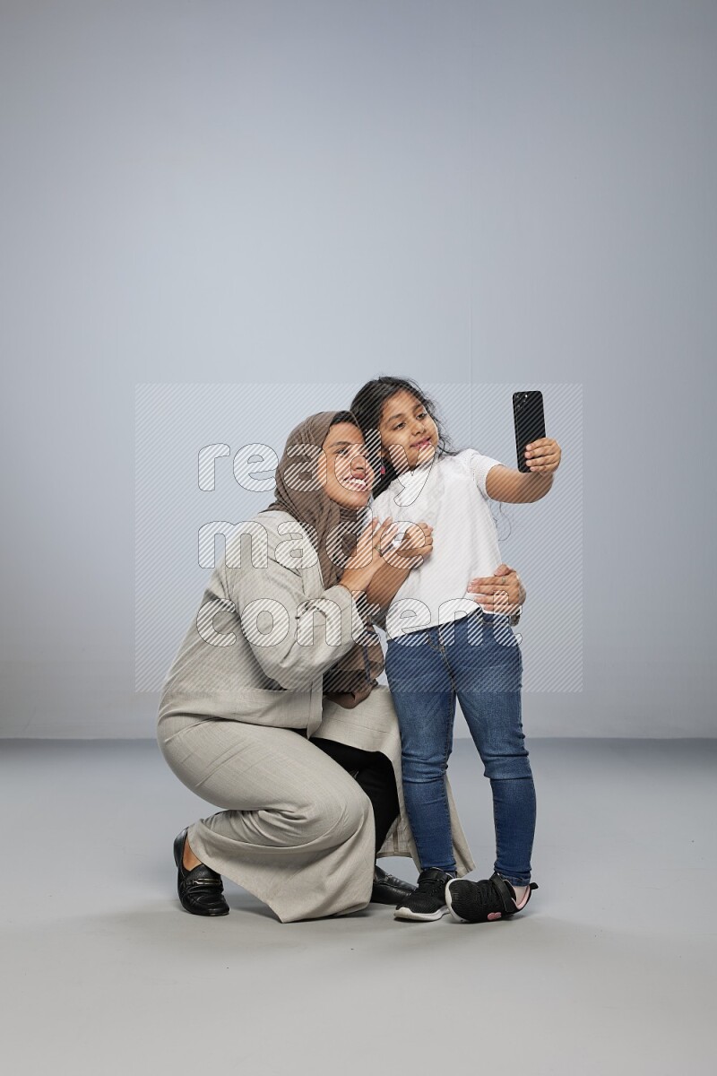 A girl standing taking selfie with her mother on gray background