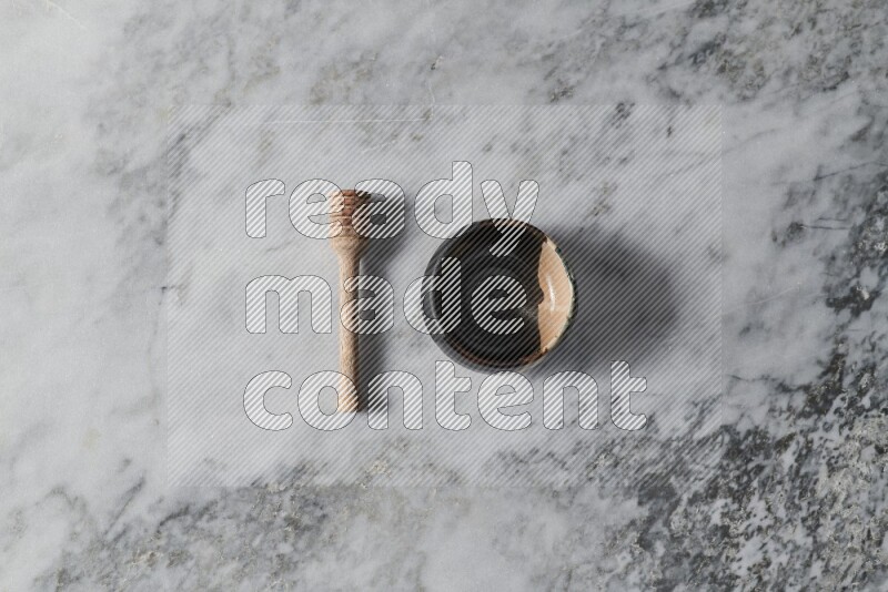 Multicolored pottery bowl with wooden honey dipper on the side on grey marble background