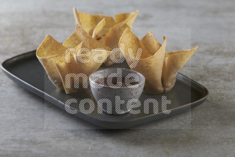 wonton cups with soy sauce ramkin on rectangle dark grey ceramic plate on grey textured counter top