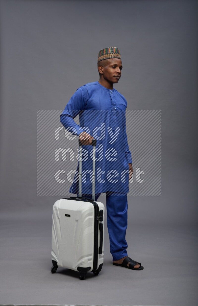 Man wearing Nigerian outfit standing holding bag on gray background
