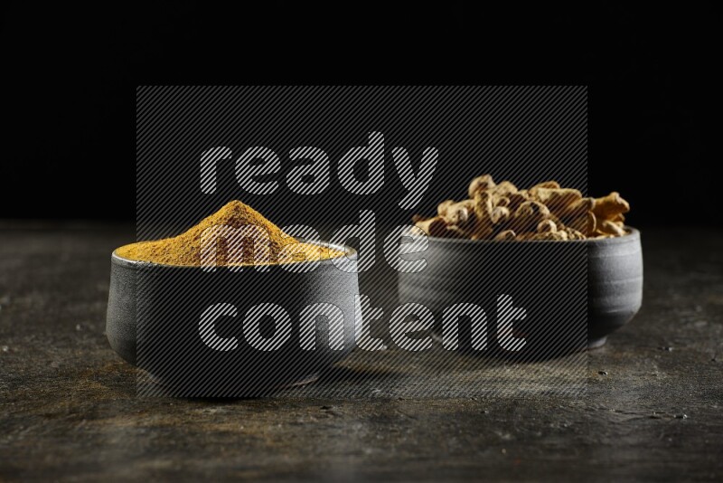 وعاءان من الفخار باللون الأسود، أحدهما ممتلئ ببودرة الكركم والآخر ممتلئ بأصابع كاملة من الكركم المجفف على خلفية سوداء