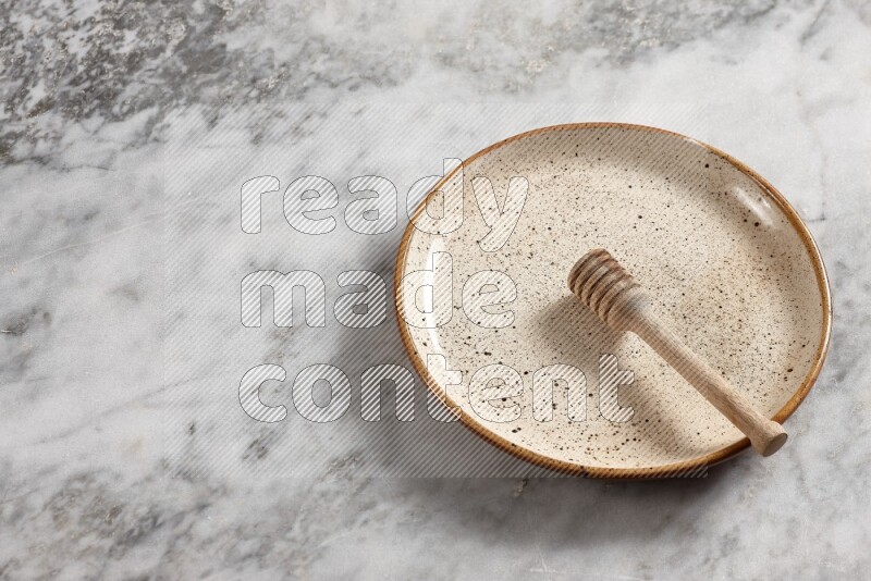 Beige pottery plate with wooden honey dipper in it on grey marble background