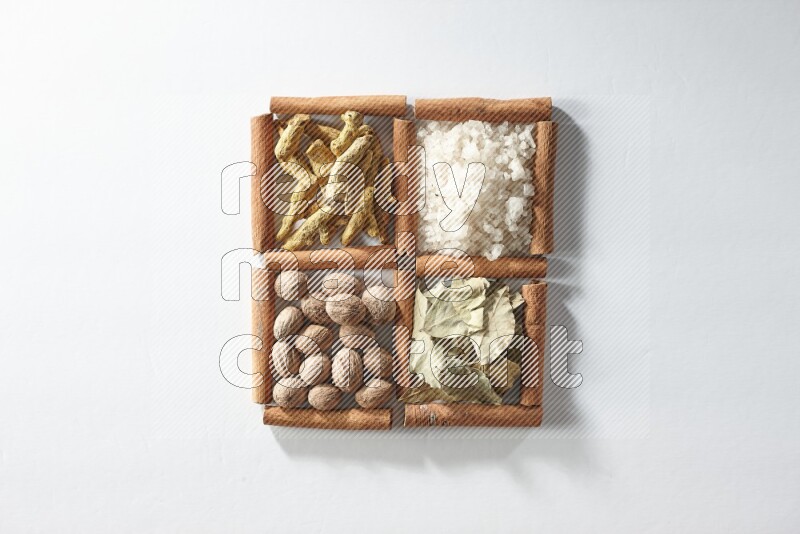 4 مربعات من أعواد القرفة ممتلئة بالملح وورق الغار وجوزة الطيب والكركم على أرضية بيضاء