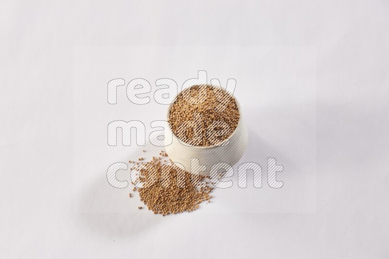 وعاء بيج فخاري ممتلئ ببذور الخردل مع المزيد من البذور المتناثرة علي خلفية بيضاء