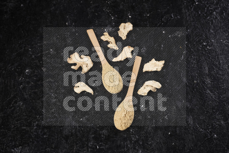Two wooden spoons full of ground ginger powder on black background