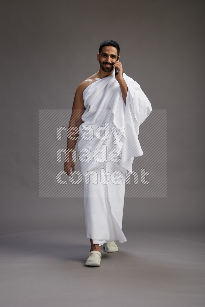 A man wearing Ehram Standing talking on phone on gray background