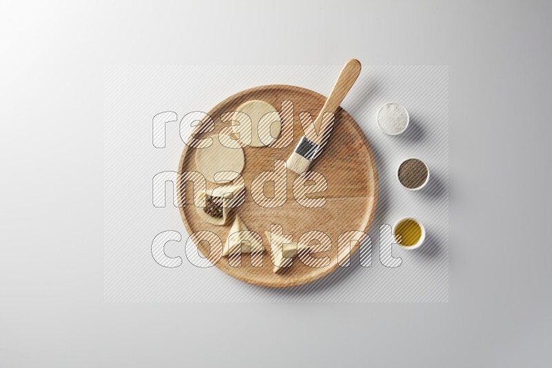 two closed sambosas and one open sambosa filled with meat while salt, black pepper and oil with oil brush aside in a wooden dish on a white background