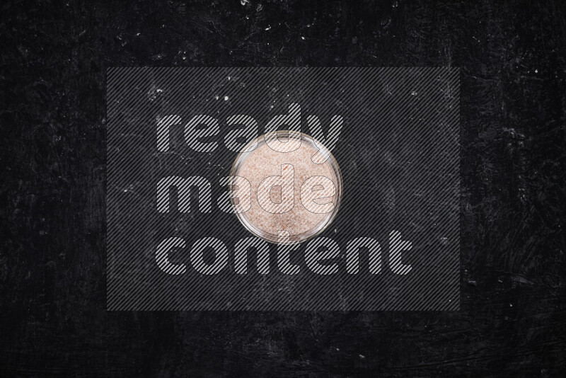 A glass jar full of fine himalayan salt on black background