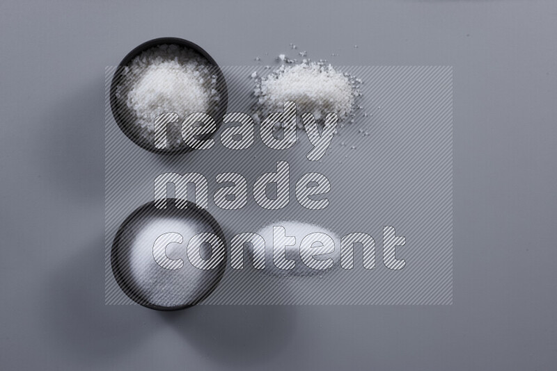 2 وعاء فخاري احدهمها ممتلئ بملح الطعام الأبيض والأخر بملح البحر الخشن على خلفية رمادية