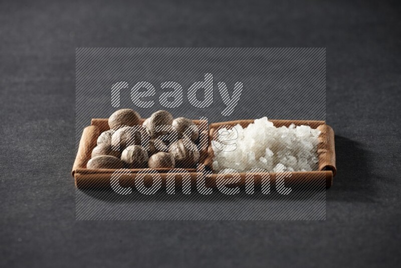 مربعان من أعواد القرفة ممتلئان بجوزة الطيب والملح الأبيض علي خلفية سوداء