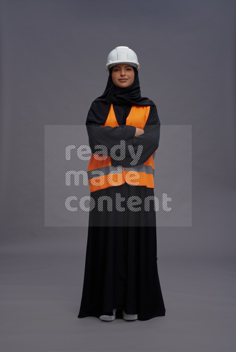 Saudi woman wearing Abaya with engineer vest standing with crossed arms on gray background