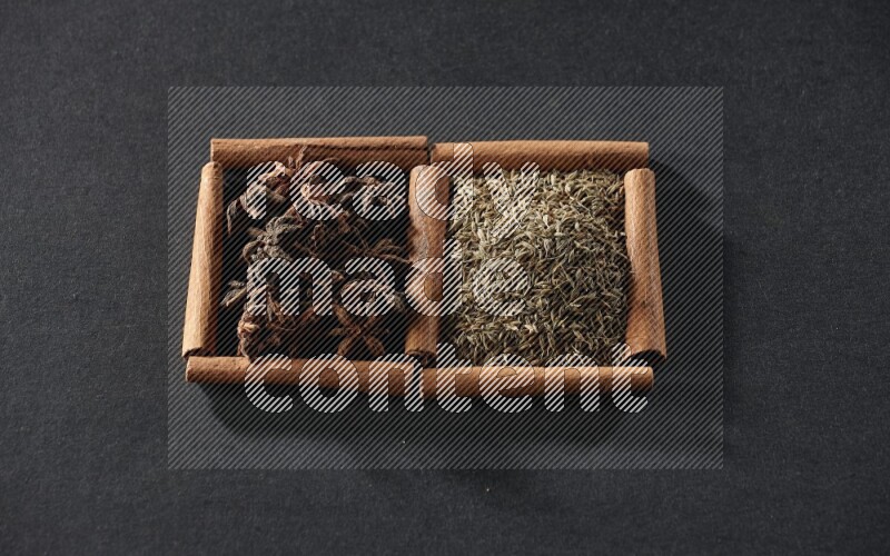 مربعان من أعواد القرفة ممتلئان بحبوب الكمون واليانسون النجمي علي خلفية سوداء