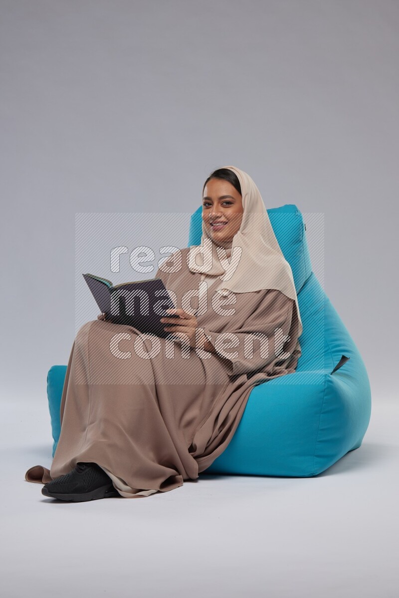 A woman sitting on a blue beanbag and reading a book