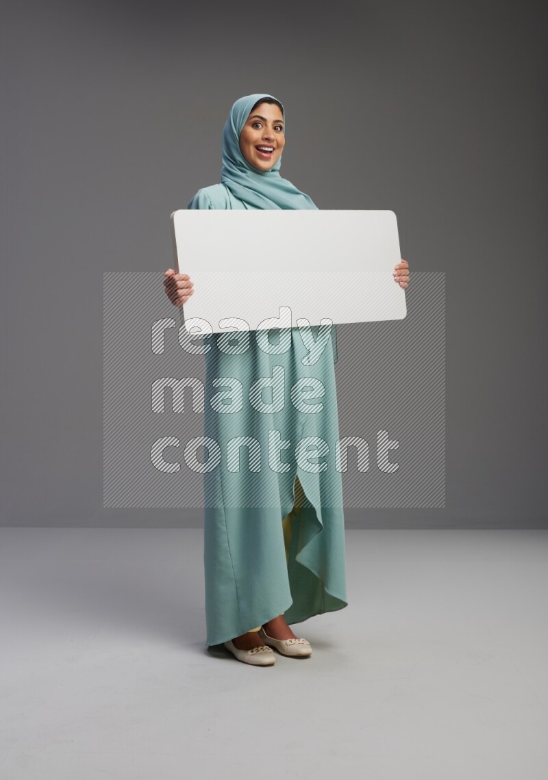 Saudi Woman wearing Abaya standing holding board on Gray background