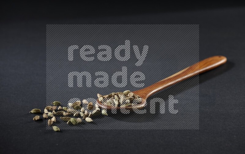 مغرفة خشبية ممتلئة بالهيل على خلفية سوداء