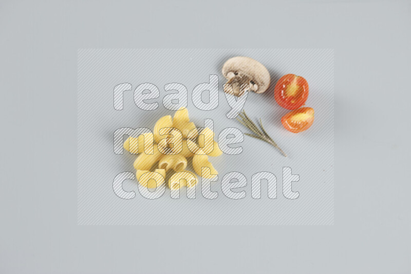 Raw pasta with different ingredients such as cherry tomatoes, garlic, onions, red chilis, black pepper, white pepper, bay laurel leaves, rosemary, cardamom and mushrooms on light blue background