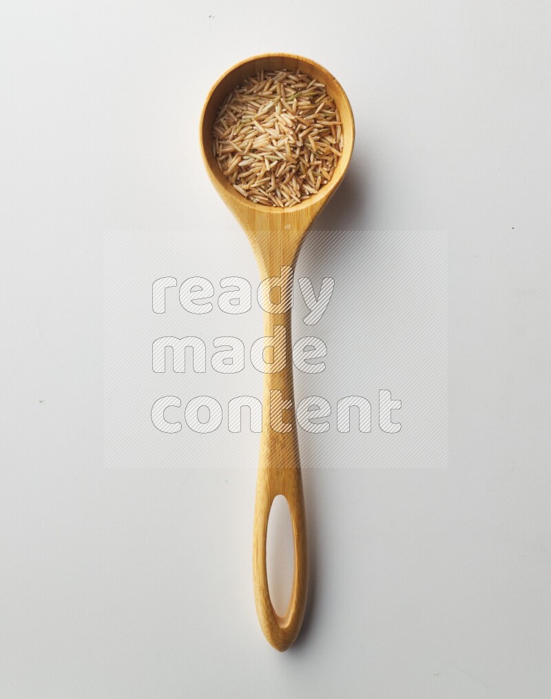 Top-view of a long grain brown rice inside a wooden spoon on white background