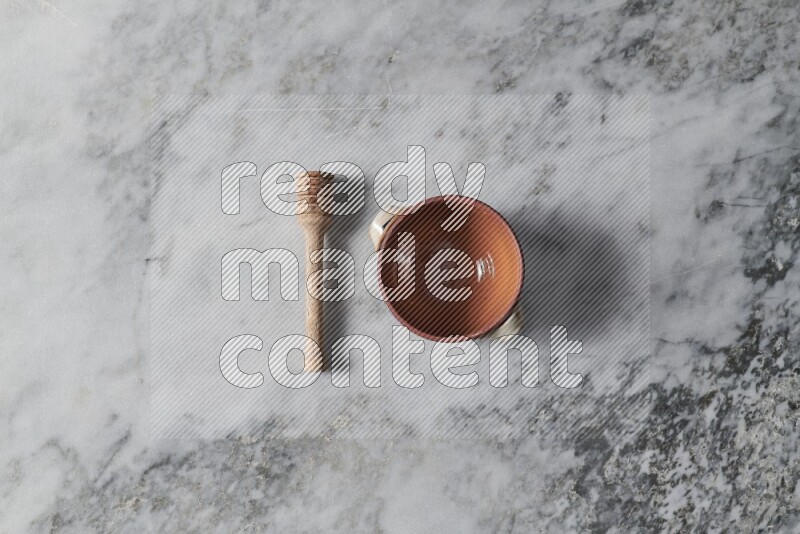 Brown pottery bowl with wooden honey dipper on the side on grey marble background