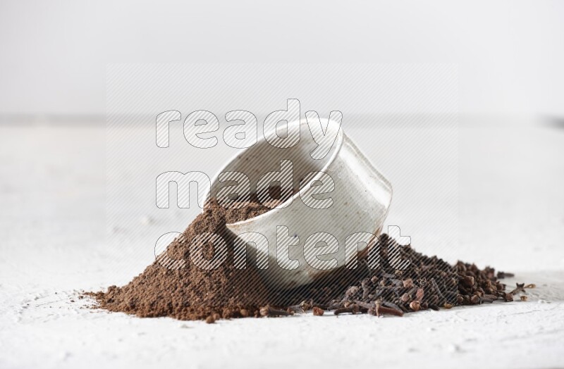 A beige ceramic bowl with cloves powder spilled out of it on a textured white flooring