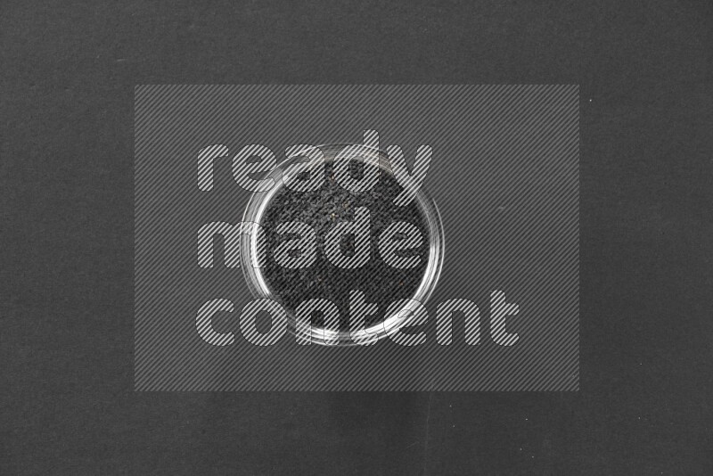 A glass bowl full of black seeds on black flooring