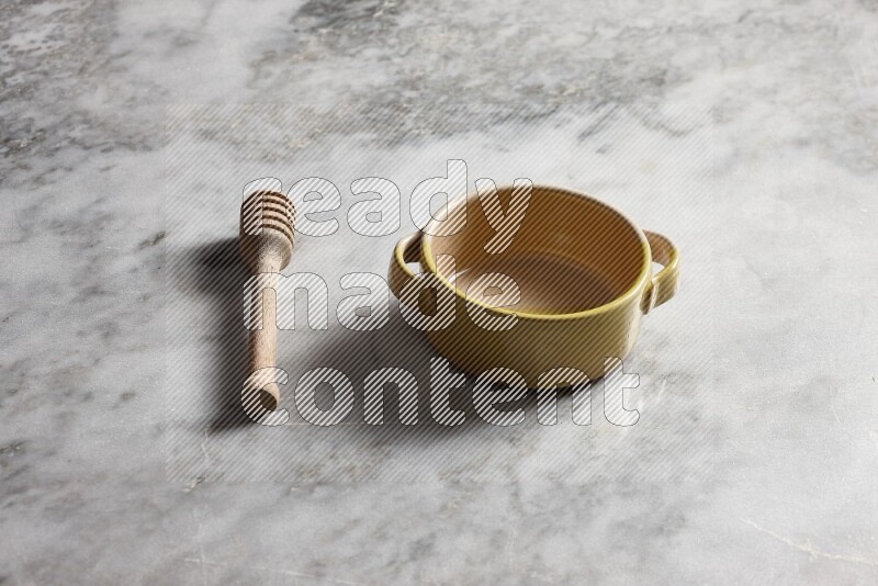 Multicolored pottery bowl with wooden honey dipper on the side on grey marble background