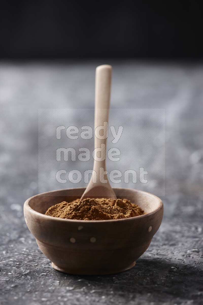 Wooden bowl full of cinnamon powder with a wooden spoon on a textured black background in different angles