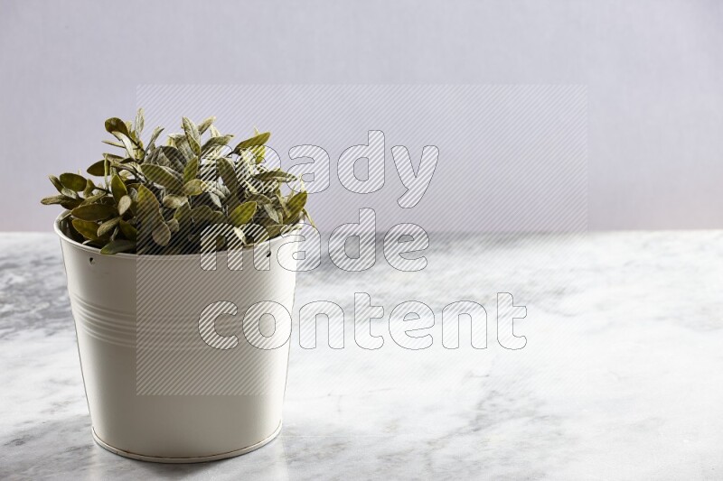 Green artificial plant in white pot on light grey marble background