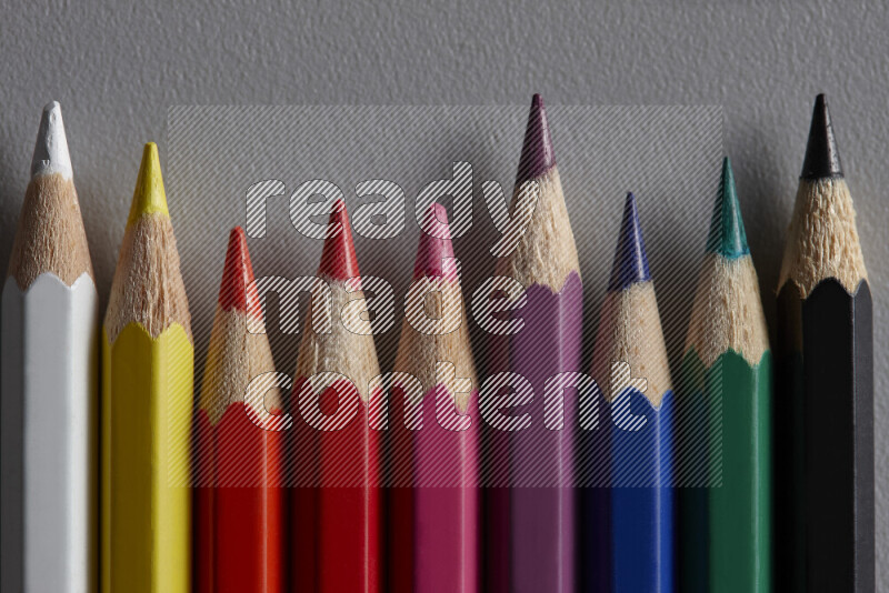 A collection of colored pencils arranged showcasing a gradient of different hues on grey background