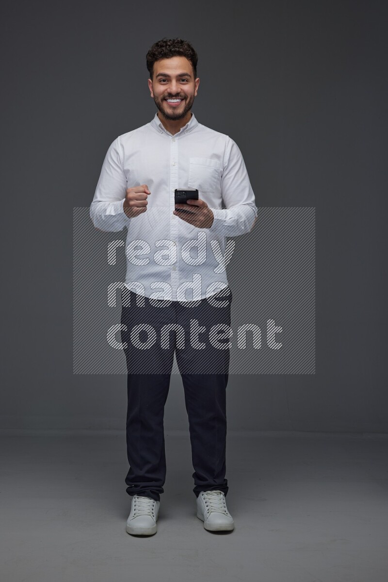 A man wearing smart casual standing and using his phone eye level on a gray background