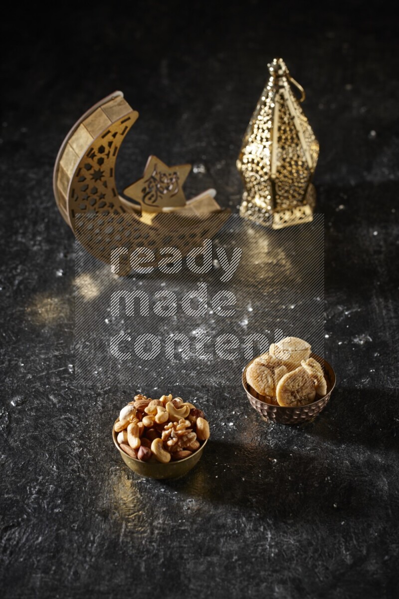 Nuts in a metal bowl with dried figs beside golden lanterns in a dark setup