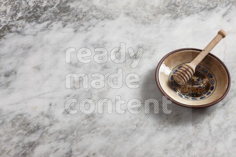 Decorative pottery plate with wooden honey dipper in it on grey marble background