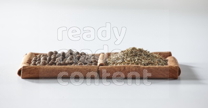 مربعان من أعواد القرفة ممتلئان ببهار الفلفل الحلو والكمون علي خلفية بيضاء