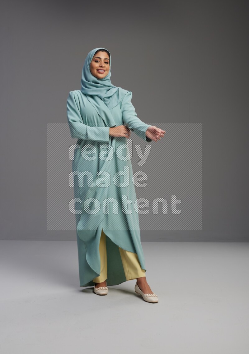 Saudi Woman wearing Abaya standing interacting with the camera on Gray background