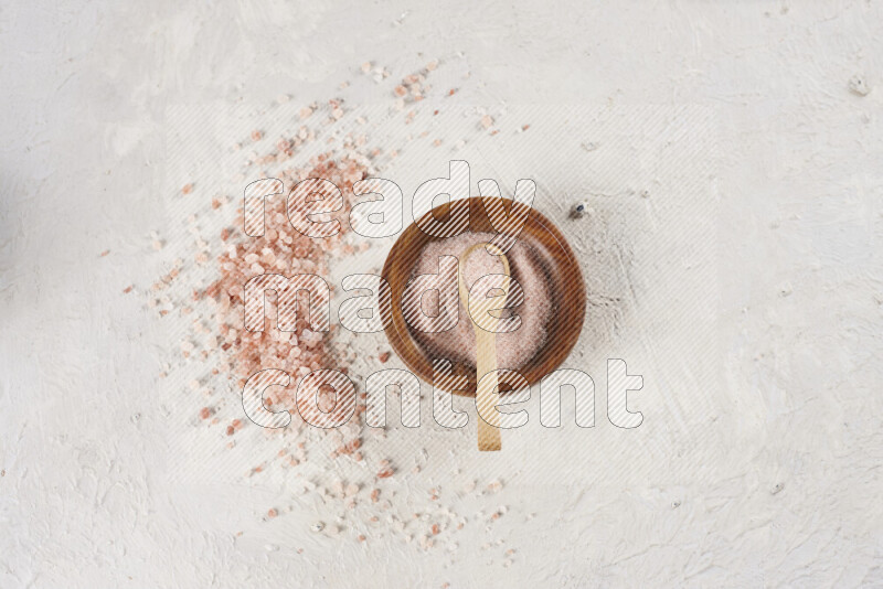 A pottery plate full of fine salt with bunch of coarse salt beside it on white background